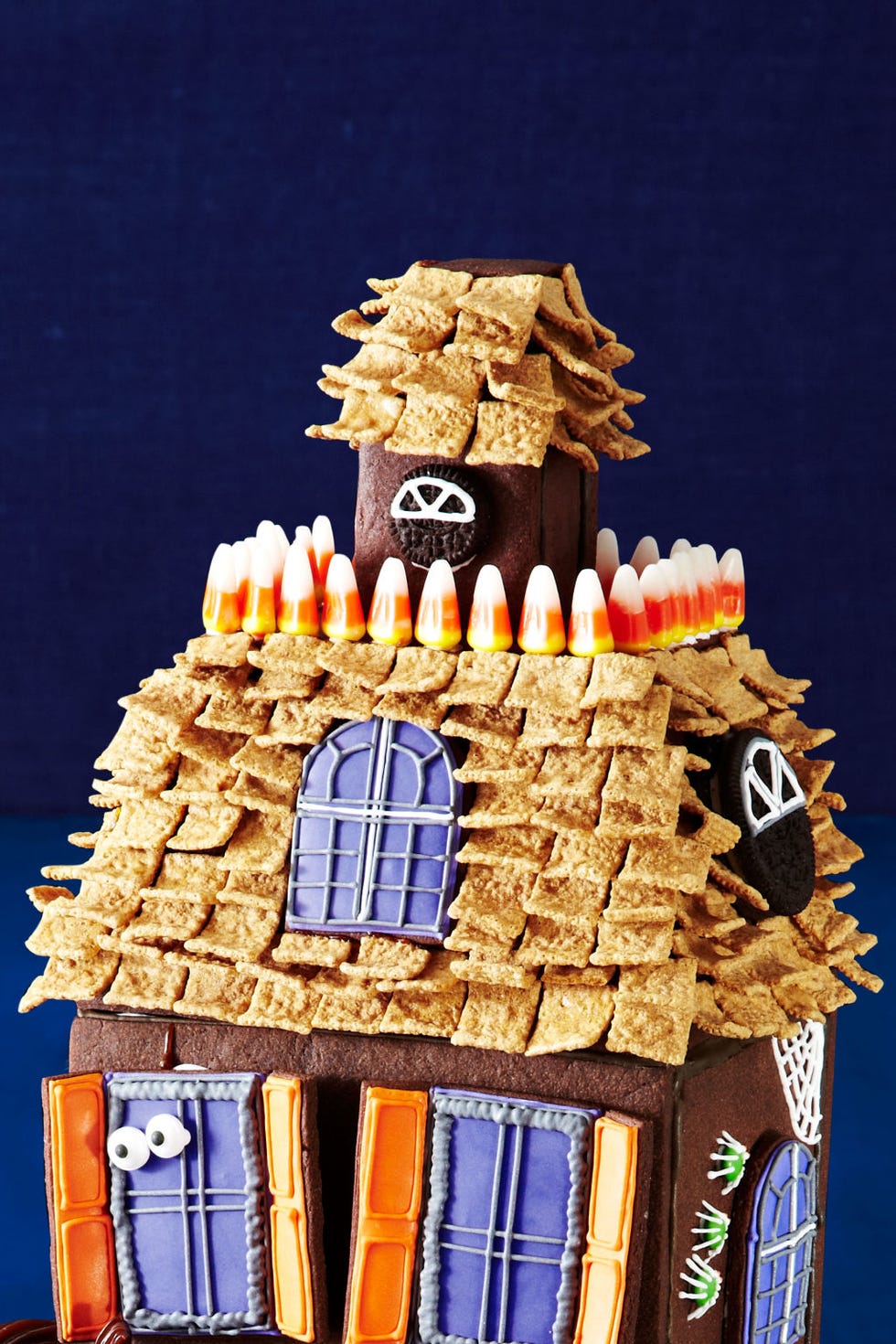 <p><strong>Window and porthole:</strong> Using royal icing, pipe windowpanes on a regular and mini Oreo cookie. Attach to sides of roof and attic with royal icing.</p>
<p><strong>Balcony railing:</strong> Use royal icing to stick candy corn around the roof as shown.</p>
