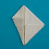 Fold the side corners in so they meet in the center, but don't fold exactly straight. Pull up above the center point, and you'll start to see the ears shape up. The napkin will form a kite shape.