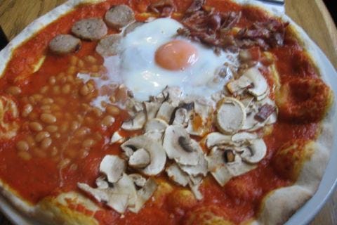 <p>With its sausage, baked beans, fried eggs, bacon, potatoes, mushrooms, and tomato, the full English breakfast is hearty and filling… though not necessarily when you put it all on a pizza! Lump it all on a crusty-pizza base and top it all off with cheese, and you have a surprisingly popular British meal. </p>