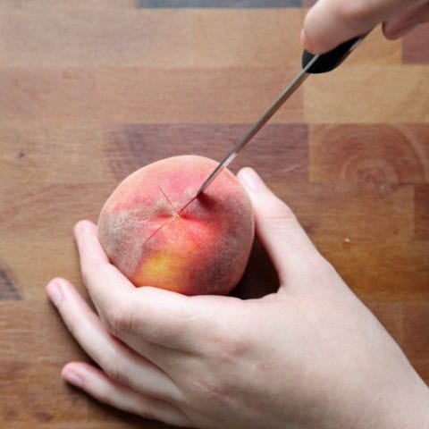 <p>Use a sharp paring knife to score the skin, by making a very shallow cut (avoid marring the flesh as much as possible) into the pointed end of each peach, in an x-shape. This will aid the peeling process later on.</p>