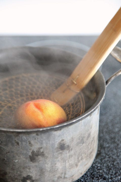 <p>Dunk the peaches into a bath of simmering water that is deep enough to submerge them completely. If the peaches do not stay submerged, turn them occasionally, so that they are heated evenly. After about 40 seconds (a minute if they're slightly underripe), or when the skin begins to slightly pull away on the scored ends, remove the peaches with a slotted spoon or skimmer.</p>