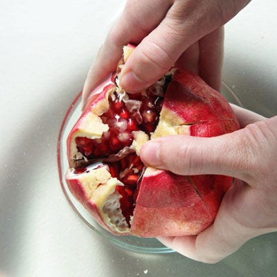 Fill a large bowl with warm water. Submerge the pomegranate in the water bath (this will contain juice splatter should any seeds rupture), and gently crack it open along the score lines, pulling each section of flesh outward. If this step proves troublesome, extend the score lines further into the flesh and try again.