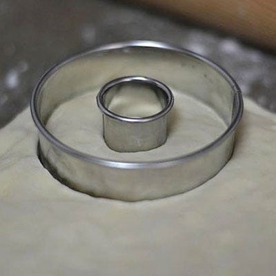 Use two different-sized ring molds to make a donut shape out of the dough. We tried frying the cronut holes, but unfortunately they fell apart instantly once they hit the oil. Cut out all of the cronut shapes. If the dough is getting too sticky, put it back in the refrigerator and chill for a few minutes.