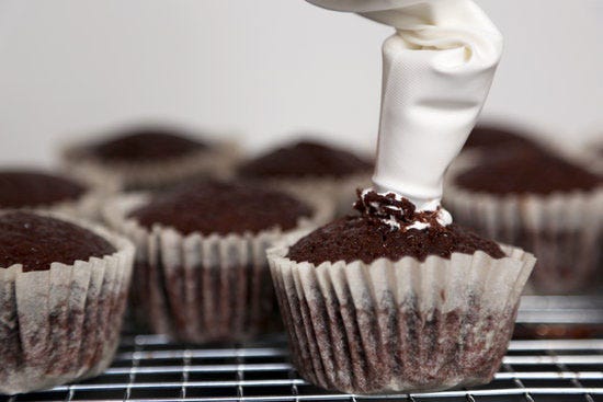 To fill the cupcakes, simply dive the star tip of the pastry bag into each cupcake's center. To make sure you fill each cupcake with the same amount, twist off a small section of the pastry bag (toward the tip) and only squeeze that amount (or less) into the cupcake. This little technique allows you to keep everything consistent, since you can't see how much marshmallow filling is actually in the center of each cupcake.