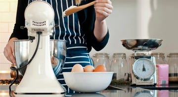 person holding a wooden spoon in front of a stand mixer