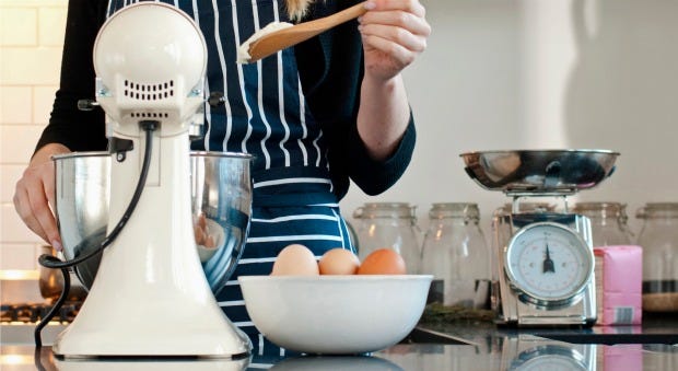 person holding a wooden spoon in front of a stand mixer