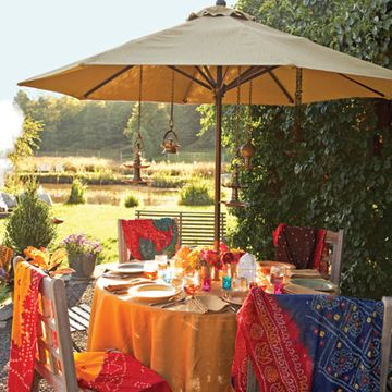 To set the mood for her cookout, cookbook author and Indian cooking authority Maya Kaimal keeps the table colorful and slightly exotic, much like the spices used to prepare the meal. A saffron tablecloth anchors a table set with jewel-toned votives, cutwork lanterns, and compact bouquets picked from the garden. When dining alfresco, Maya keeps cushions on hand to soften the seats of outdoor furniture and incorporates multiple light sources, such as paper lanterns, votives, and oil lamps. She also drapes vintage cotton shawls over each chair in case the night air gets chilly.