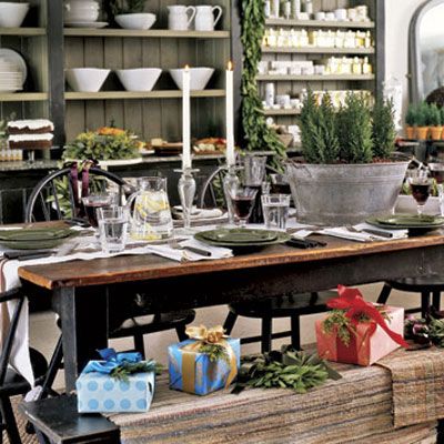 <p>A long table features an unexpected centerpiece of live miniature trees and dried rose hips in a galvanized tub. Bright gifts serve as place cards and lush garlands line exposed shelves.</p>