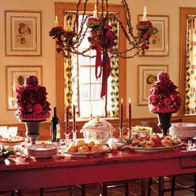 <p>This bell-shaped wrought-iron chandelier is wrapped in tendrils of greenery, ribbon flourishes, and clusters of wooden cranberries. Fleur-de-lis candlesticks and a pair of berry-studded and frosted-fruit topiaries in antique garden urns give the table layers of height.</p>