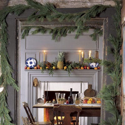 <p>Evocative and soothing, candlelight creates the right ambience for the holidays. Lit candles are more than decorative objects, highlighting seasonal festivities and fostering a celebratory mood. Garlands around the door frame beckon guests into the room and on the mantel sits a pineapple, an early-American symbol of hospitality.</p>