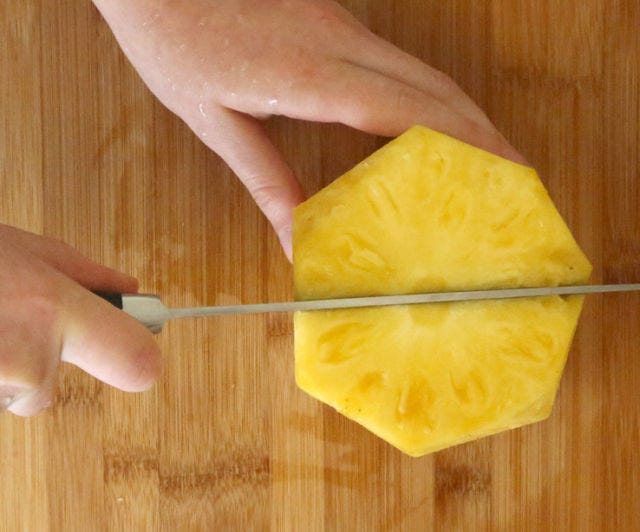 <p>Next, cut the pineapple down the center.</p>