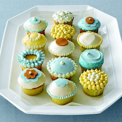 a plate of yellow, blue, and white frosted cupcakes with sprinkles and decorations