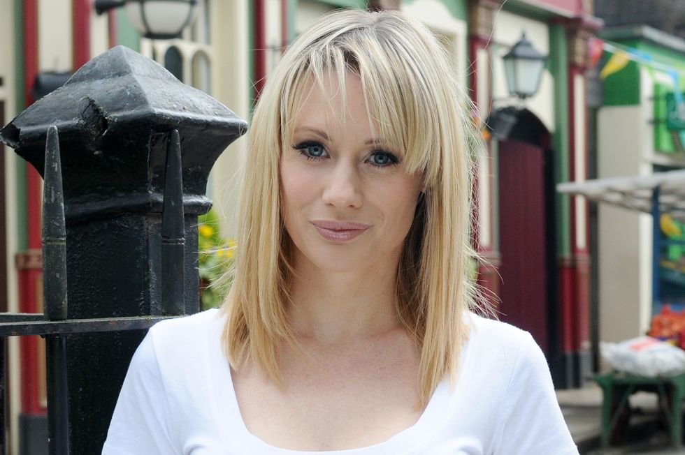kellie shirley as carly wicks in eastenders standing against the railings in jeans and a t shirt