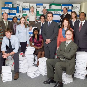 the office us cast group shot, with people either standing or sitting on stacks of paper