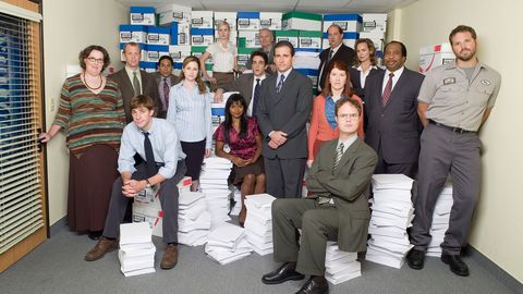 la foto de grupo del elenco de la oficina, con personas de pie o sentadas en pilas de papel