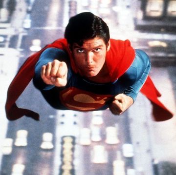 actor christopher reeve as superman flying through the air in his iconic blue and red superhero costume with a red cape