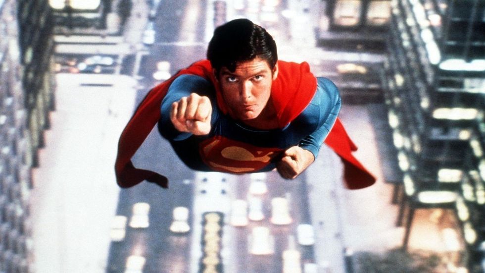 Schauspieler Christopher Reeve als Superman, der in seinem ikonischen blau-roten Superheldenkostüm mit rotem Umhang durch die Luft fliegt