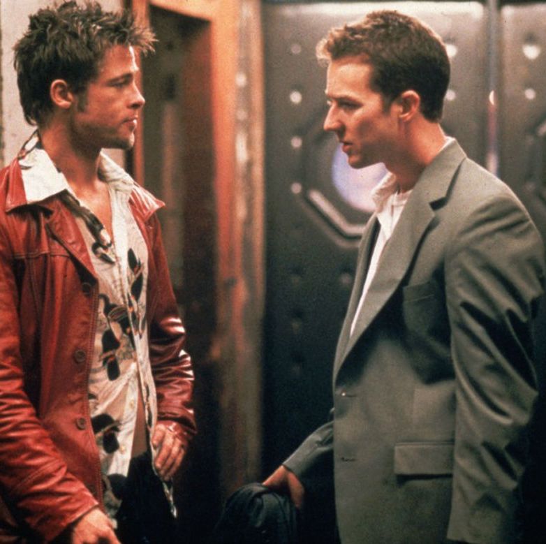 fight club's brad pitt and ed norton facing each other, with pitt in his iconic leather jacket and norton in a grey suit