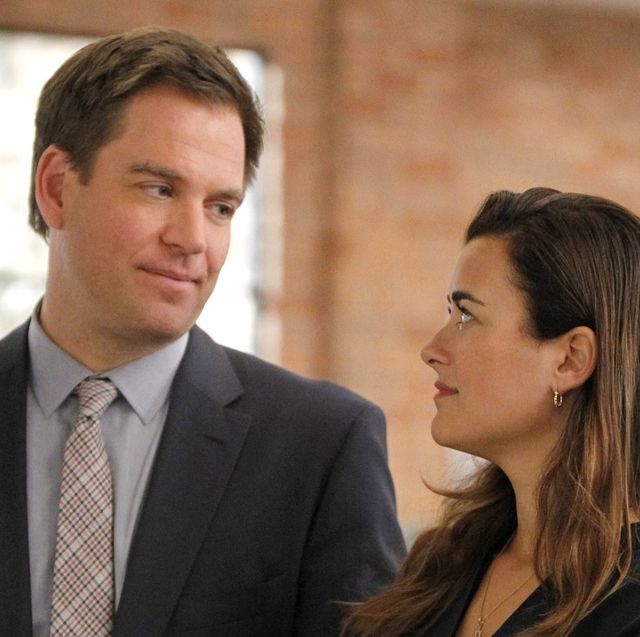 dinozzo and ziva in ncis, standing close and sharing a smirk in an indoor environment