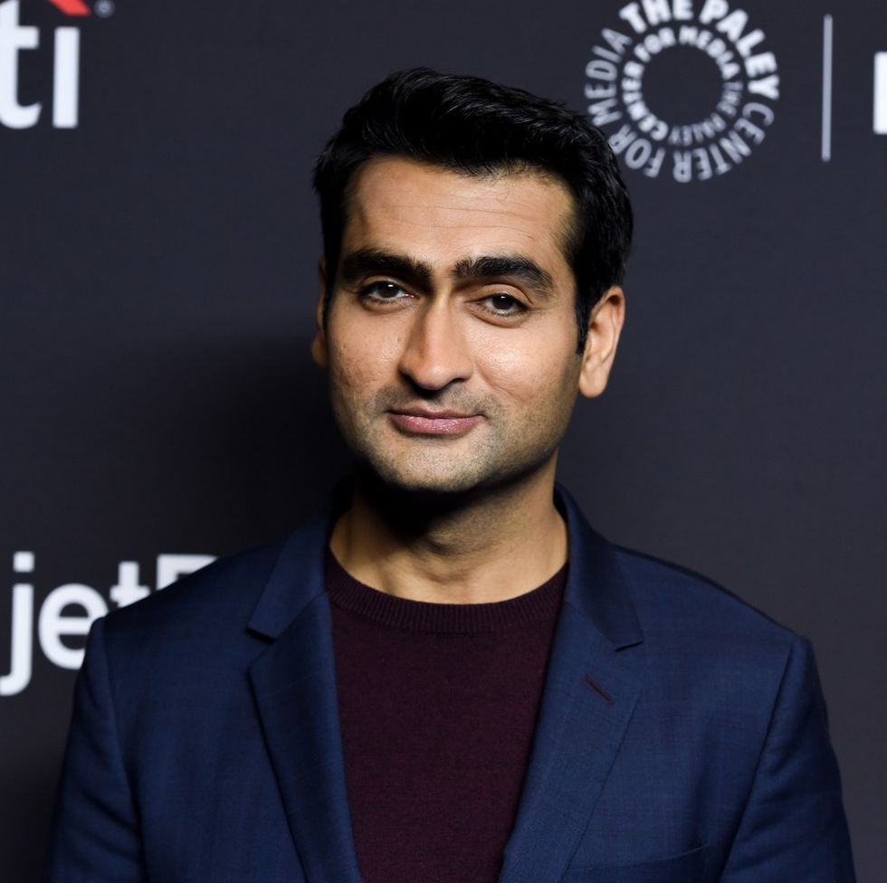 kumail nanjiani, wearing a blue suit jacket and red jumper, at a red carpet event