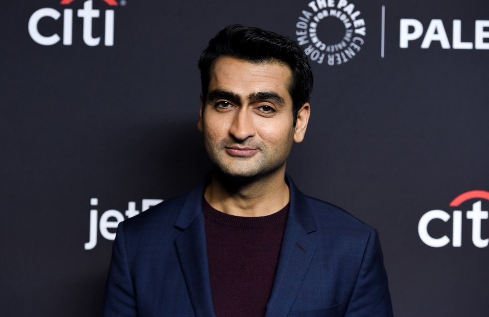 kumail nanjiani, wearing a blue suit jacket and red jumper, at a red carpet event