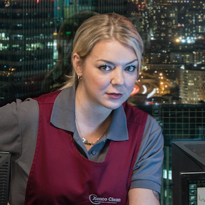 cleaning up on itv, sheridan smith in an apron with a vacuum cleaner in a london high rise office