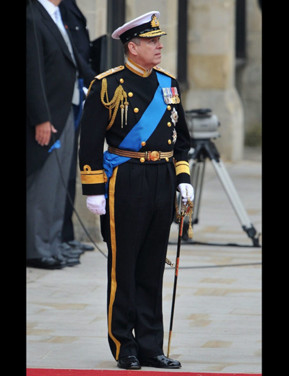 Standing, Hat, Formal wear, Headgear, Uniform, Blazer, Street fashion, Peaked cap, Fashion design, Suit trousers, 