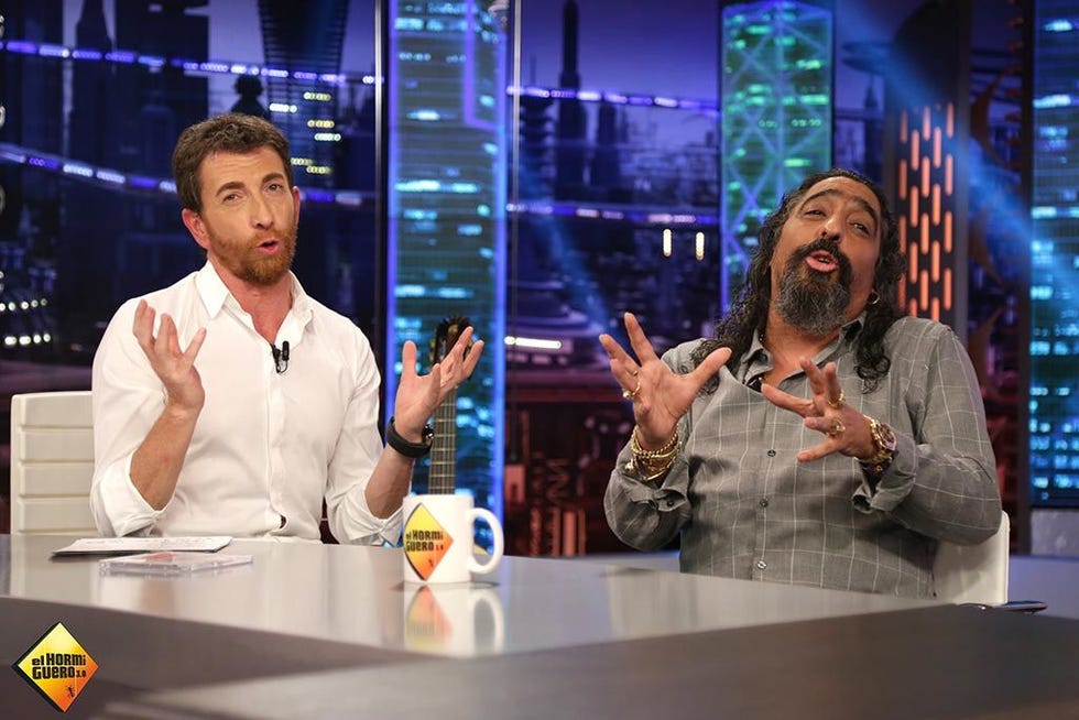 Arm, Table, Logo, Transparent material, Spokesperson, Facial hair, Display device, Speech, Beard, Television program, 