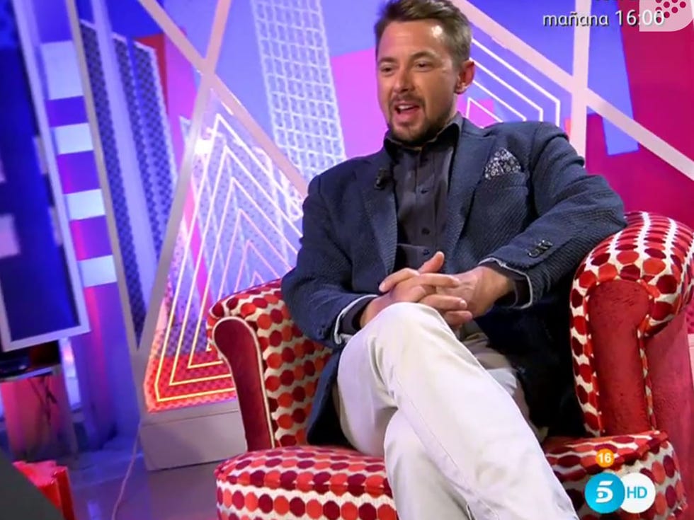 Human body, Sitting, Blazer, Lap, Living room, Suit trousers, Television program, Lamp, Throw pillow, Armrest, 