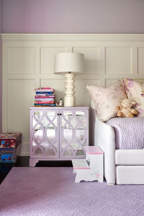 In Carmen's room, creamy white wainscoting offers a strong, sophisticated counterpoint to the more dainty lavender textiles found throughout the space. A mirrored nightstand is from Lillian August.