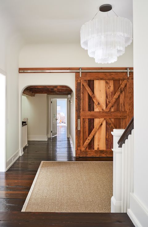 The hallway outside of Alec and Hilaria's master bedroom epitomizes the home's farmhouse-meets-transitional style with a reclaimed barn door and a chunky selenite chandelier by Ron Dier.