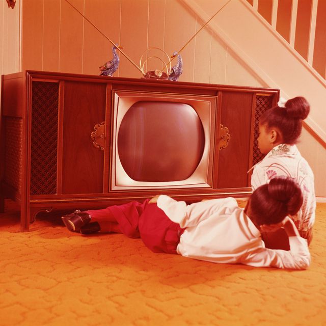 Two girls on living room floor, watching television.