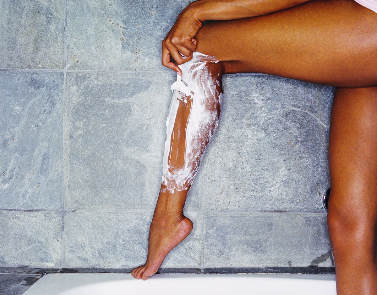 woman shaving legs with shaving cream and razor