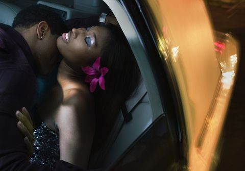 Young man kissing young woman in back seat of car, night