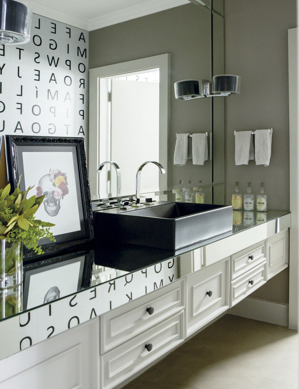 <p>Una &quot;sopa de letras&quot; decora una de las paredes del baño y se refleja sobre el mueble de lavabo negro, revestido con superficies de espejo.</p>