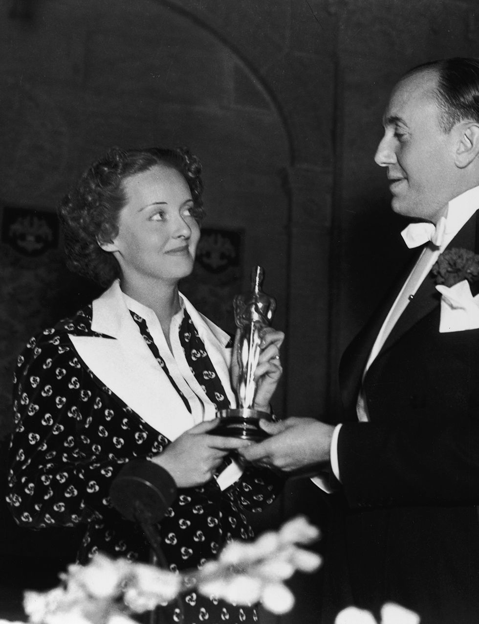 <p>La que sería una de las grandes estrellas de la época dorada de Hollywood subió a recoger su primer Oscar por 'Peligrosa' (Alfred E. Green, 1935), en la que daba vida a una actriz alcohólica. Vistió un vestido estampado con flores y maxisolapas de <strong>Orry Kelly,</strong> un reputado diseñador de vestuario de la época.</p>