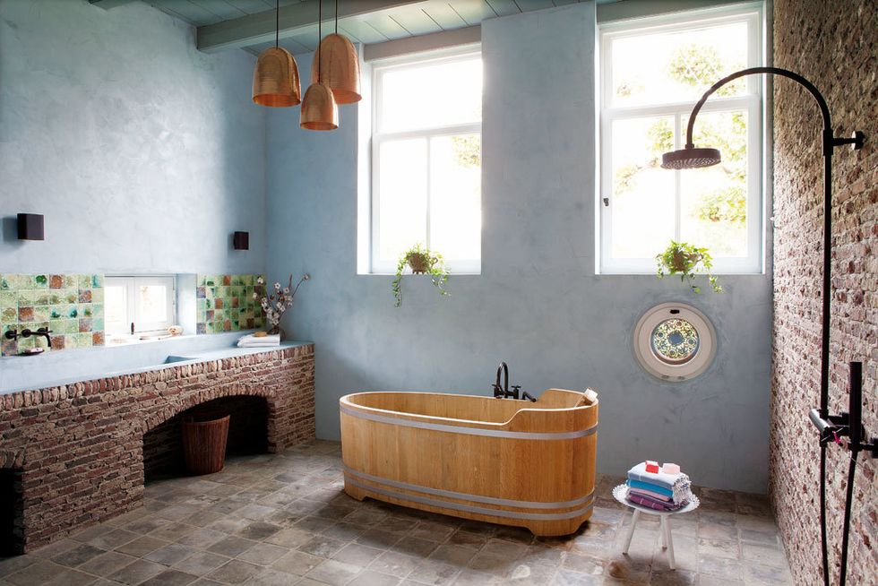 <p>Atmósfera nostálgica en un baño que apuesta por los materiales recuperados, como los ladrillos que ya estaban en la casa y revisten una pared y el mueble con lavabo. En éste se aplicó cemento pintado y tratado, y en la pared, azulejos verdes. La bañera de madera es de Baden Van Hout, con grifería Tara de Dorntbrach.</p>