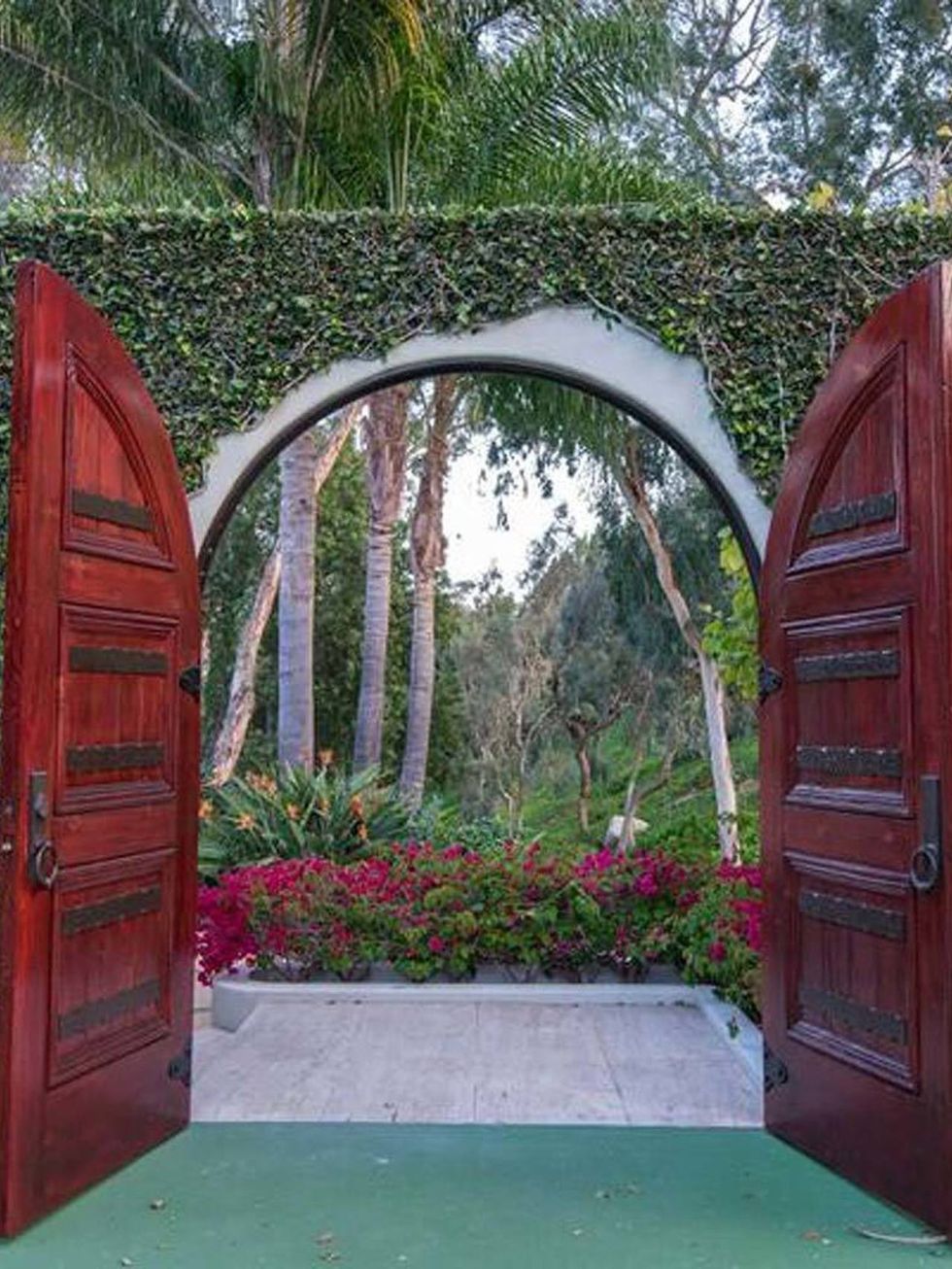 <p>La mansión cuenta con una entrada presidida por dos puertas de color escarlata y un muro cubierto por la naturaleza.</p>