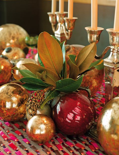 <p>Centro de mesa realizado con bolas doradas y rojas, en Becara, y varias hojas de plantas. Al lado, candelabros de estilo clásico, en Flamant.</p>