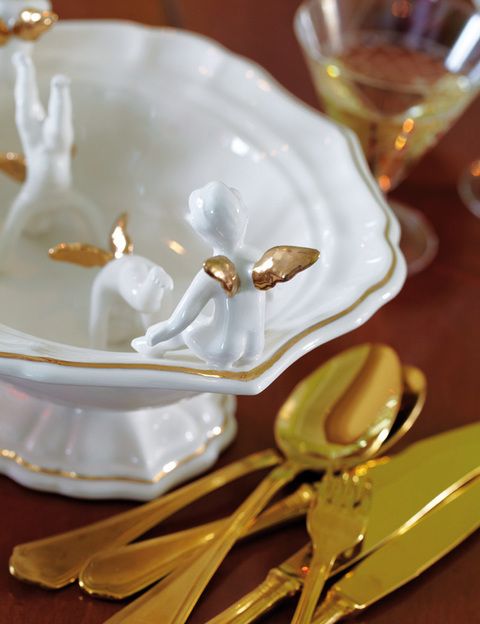 <p>Un pequeño frutero de porcelana blanca con bordes dorados y angelotes, de Paolo Polloniato. Los cubiertos de acero en color dorado son de Mepra.</p>