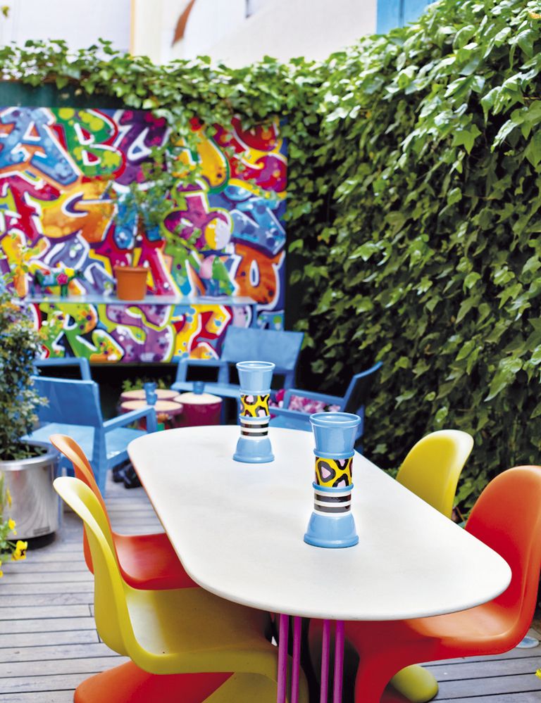 <p>Para su espacio favorito, la terraza, Antonio pintó sobre el muro con spray este graffiti e ideó a medida la mesa del comedor. Jarrones azules <i>Memphis</i> y sillas <i>Panton</i>, de Vitra.</p>