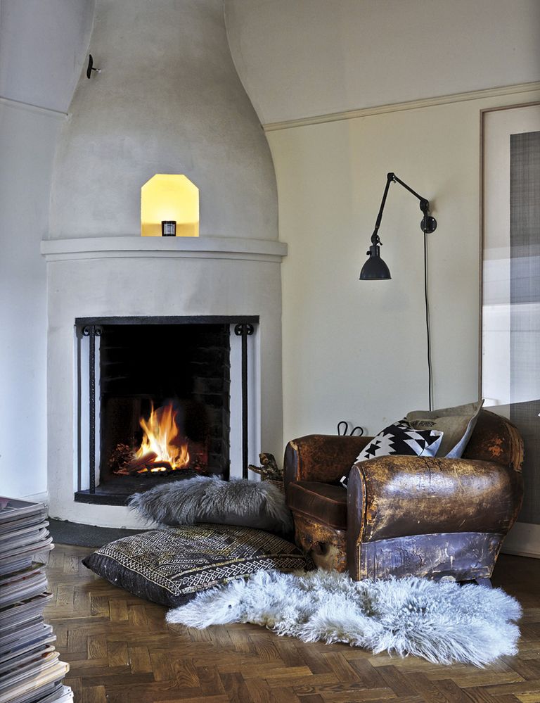 <p>Al lado de la  chimenea, un sillón de cuero  vintage con una alfombra de  pelo y maxicojines étnicos.</p>