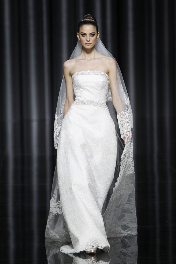 <p>Modelo &quot;Escena&quot; de <strong>Pronovias</strong>, con escote palabra de honor y ceñido a la cintura, marcada además por una simulación de cinturón bordado en color plata. El encaje, casi imperceptible sobre el vestido, llama la atención en las terminaciones del velo.</p>