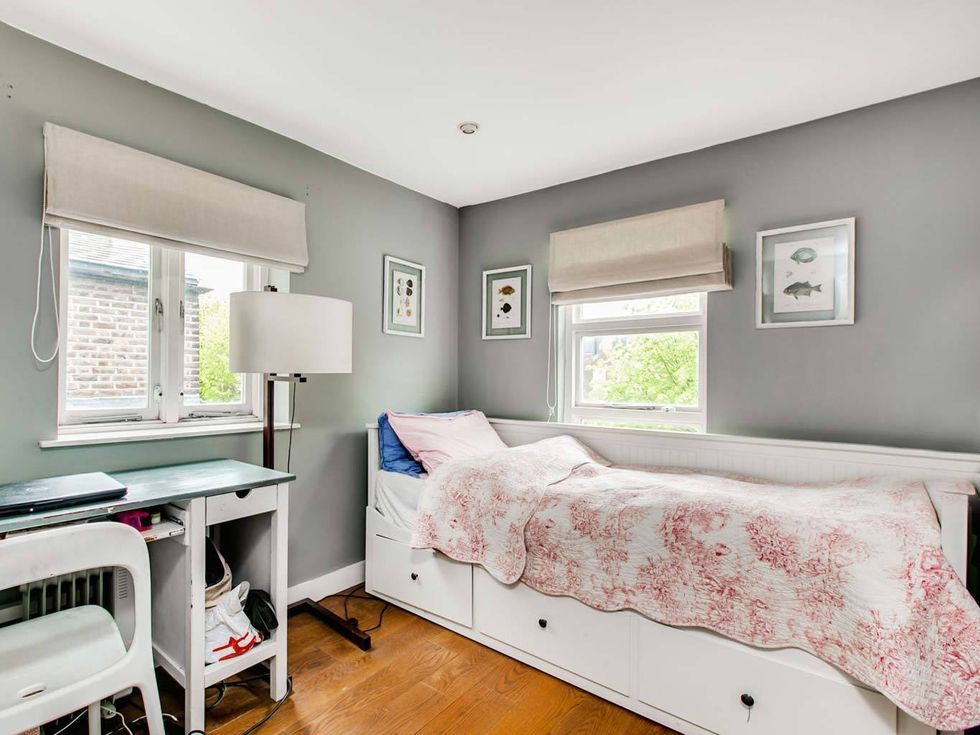 <p>Un dormitorio simple con cama individual, suelos de madera, muebles en blanco y paredes de un gris verdoso.</p>
