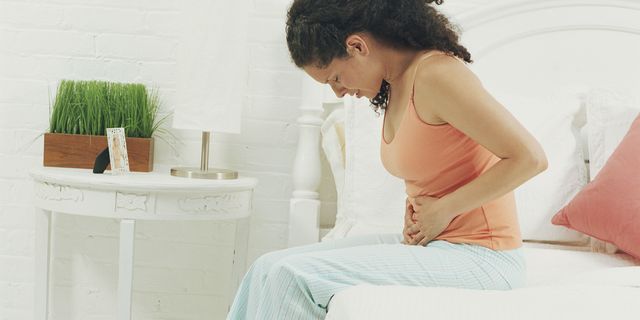 Woman sitting on bed holding stomach in pain