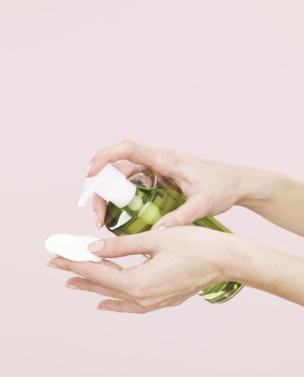 female hands, green liquid, make up remover, clear plastic bottle, dispenser, white cotton pad, pink background