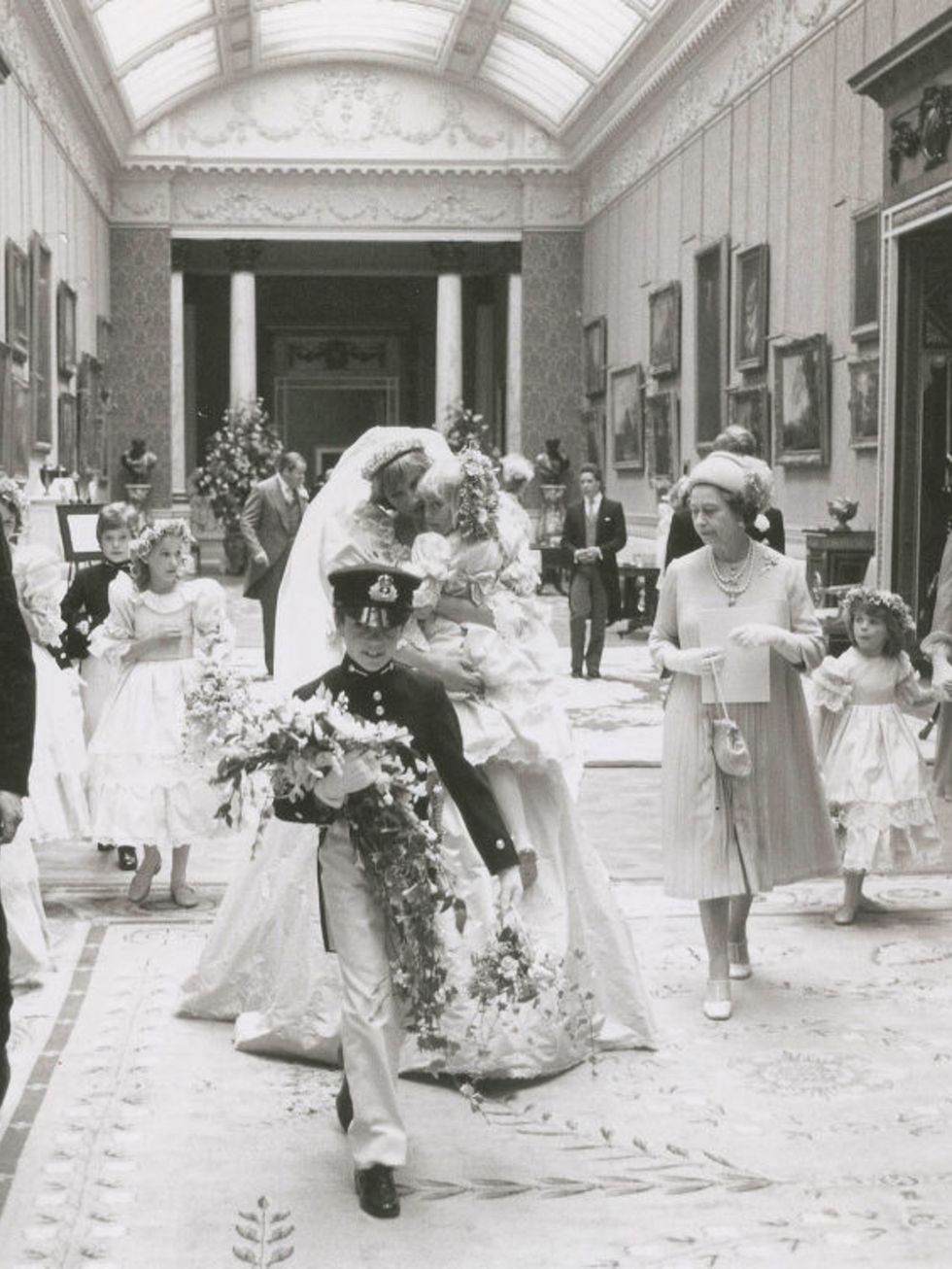 Princess Diana carries five-year-old Clementine Hambro, her youngest bridesmaid, while walking with Queen Elizabeth