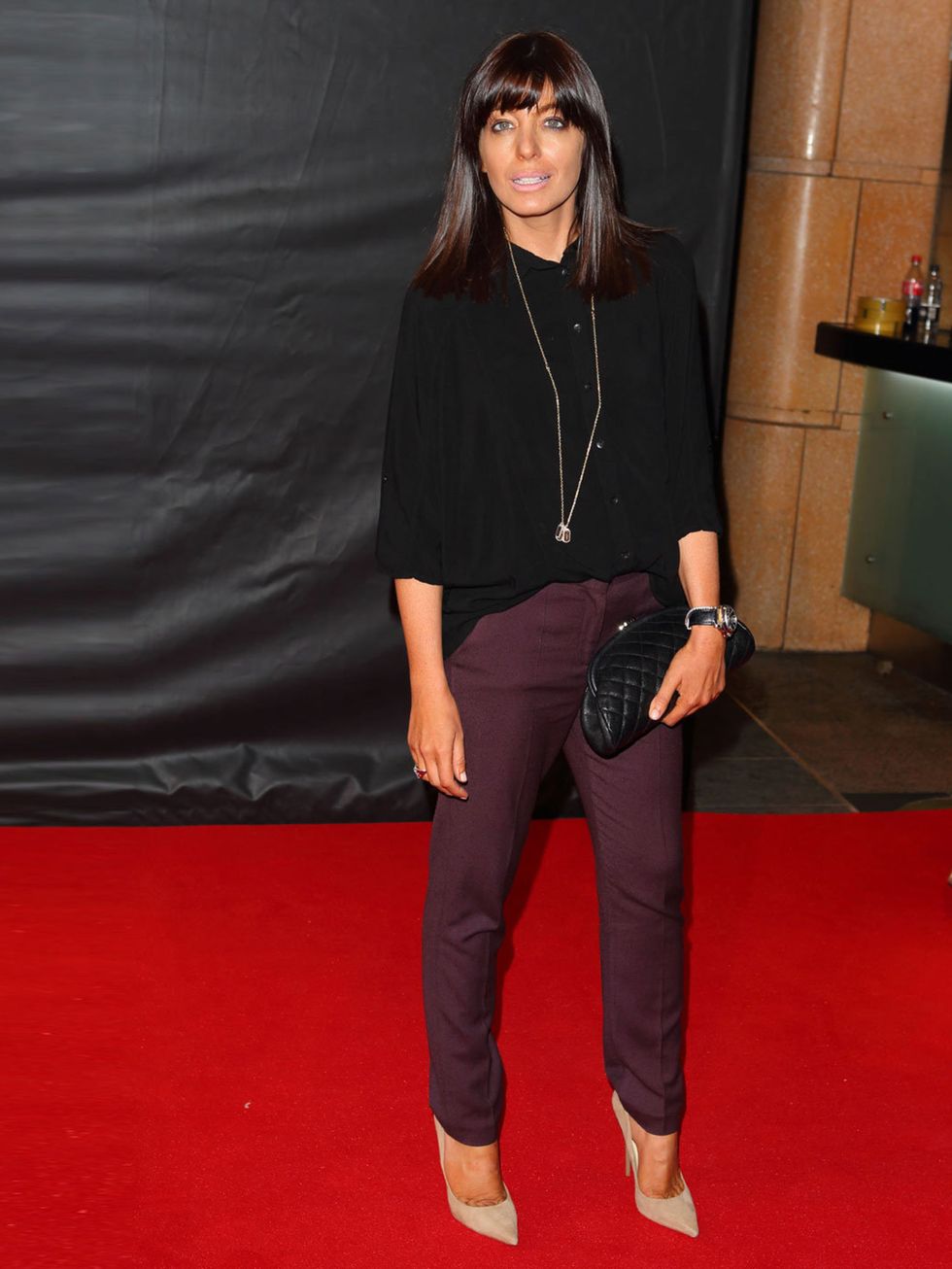 <p>Claudia Winkleman wears purple trousers, black shirt and a black quilted clutch at the Sweeney premier</p>