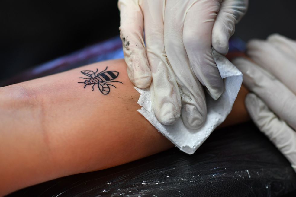 A tattoo artist inks a bee logo, synonymous with Manchester as a symbol of the city's industrial heritage, and rapidly becoming a symbol of resilience following the May 22 Manchester Arena bombing attack, at Tattitude, a tattoo parlour in Manchester, northwest England on May 26, 2017.