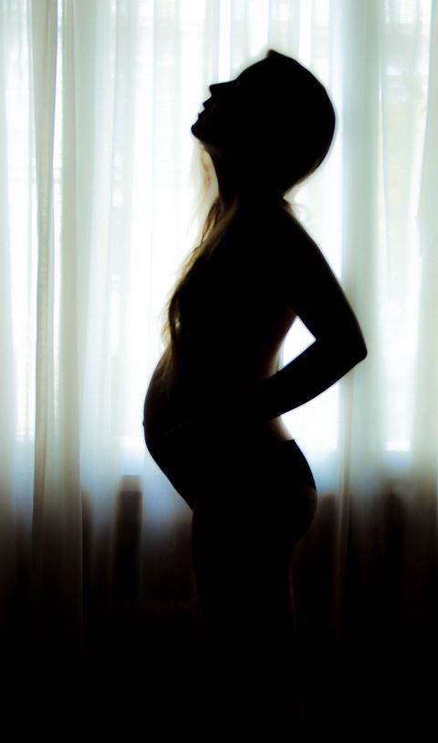 Pregnant woman by curtain window